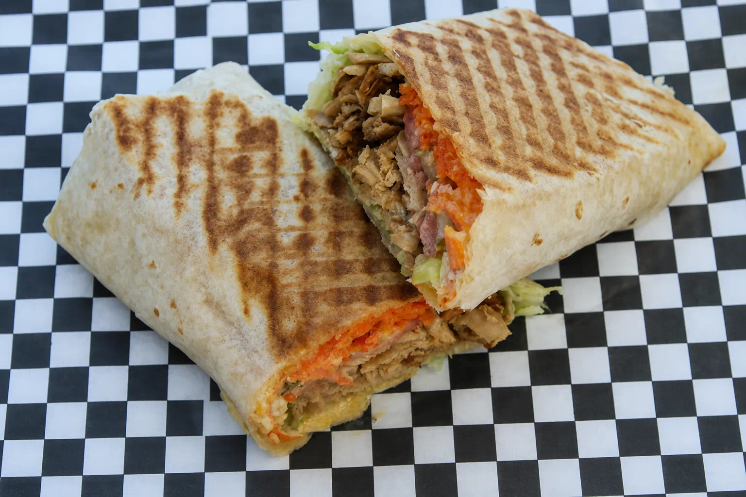 Kebab Grill shawarma wrap cut in half on checkered paper, showing grilled lavash, chicken and pickled carrot